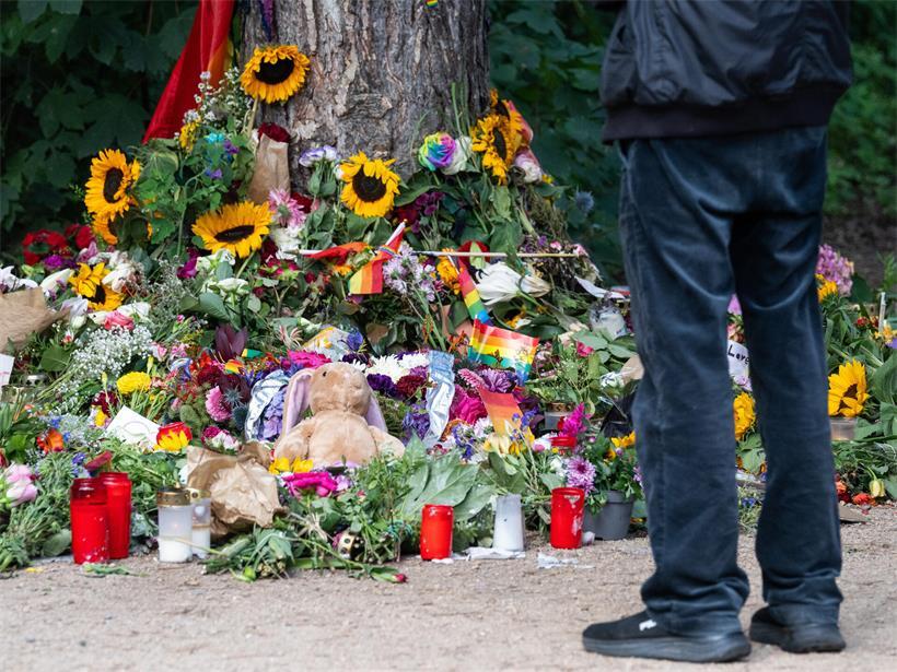 Trauernde stehen im Tiergarten an einem Baum, an dem unterschiedliche Gegenstände zum Gedenken an die Opfer des Anschlags auf den CSD abgelegt wurden