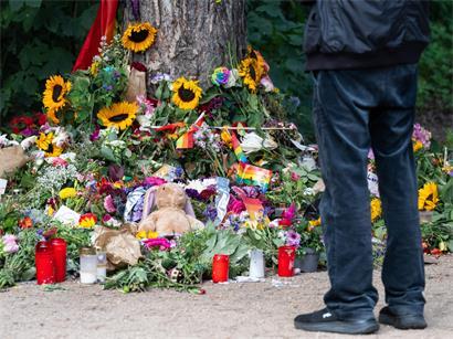  Trauernde stehen im Tiergarten an einem Baum, an dem unterschiedliche Gegenstände zum Gedenken an die Opfer des Anschlags auf den CSD abgelegt wurden