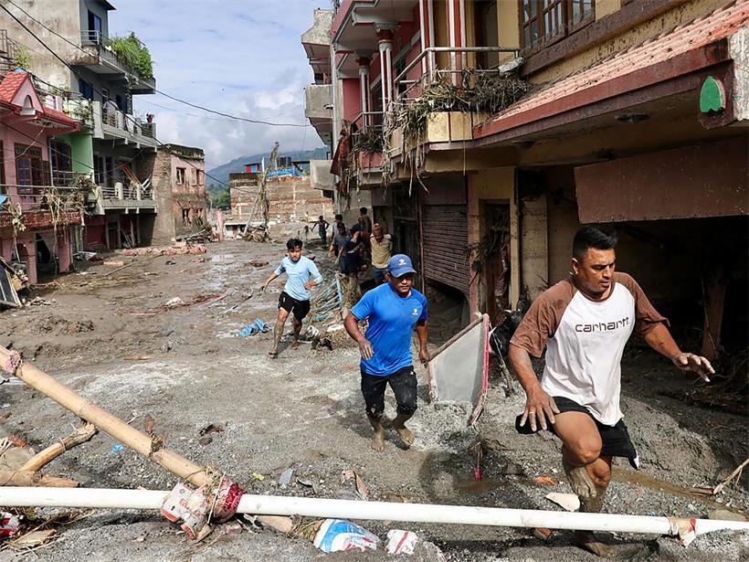 Anwohner gehen am 27. August 2026 in Devighat, Gemeinde Bidur, im nepalesischen Distrikt Nuwakot an Häusern vorbei, die nach Sturzfluten unter Schlamm begraben sind