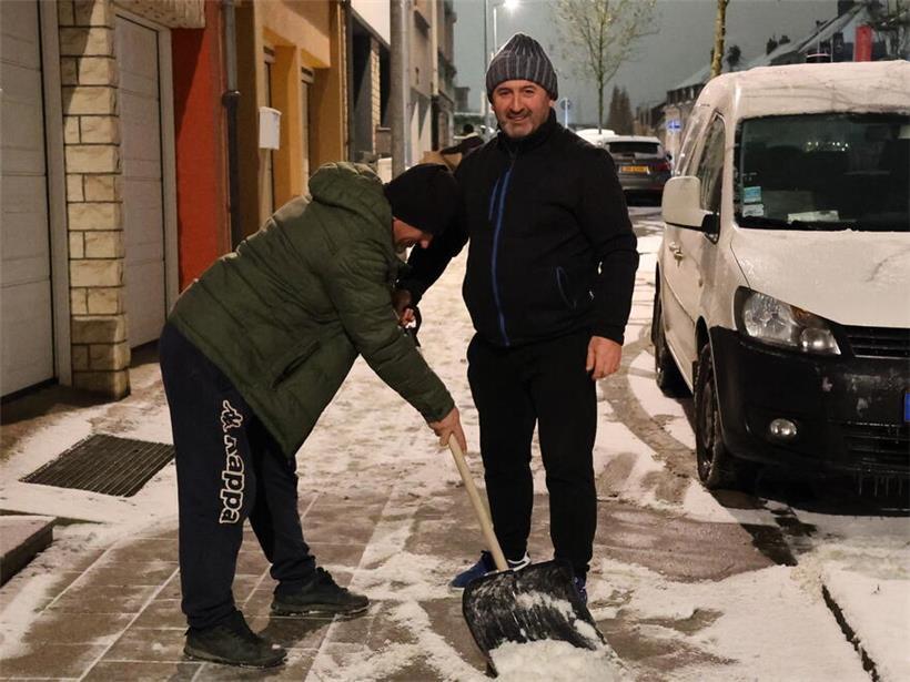 Asmir und Rahman schippen Schnee und lachen gemeinsam bei winterlicher Gartenarbeit im Freien