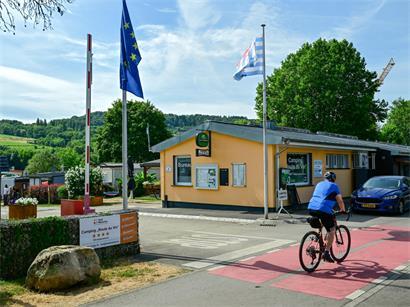 Zelt und Wohnwagen auf Campingplatz an der Weinstraße mit Weinbergen im Hintergrund bei sonnigem Wetter