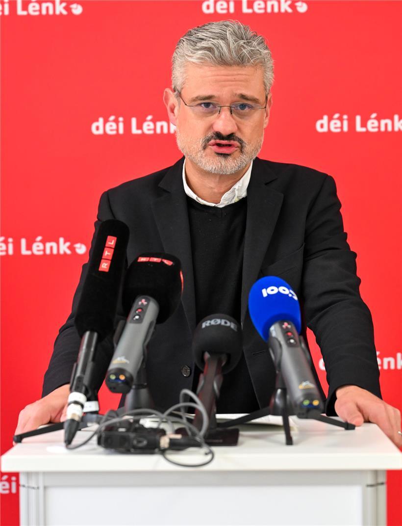 David Wagner von däi Lénk bei einer politischen Rede mit Mikrofon vor rotem Hintergrund