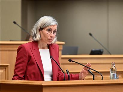Sam Tanson, Abgeordnete der Grünen Partei, spricht im Parlament vor Mikrofon und Gesetzestexten