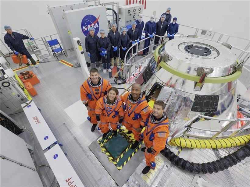 Besatzung von Artemis II: Jeremy Hansen, Christina Koch, Victor Glover und Reid Wiseman in Raumanzügen vor Raumfahrthintergrund