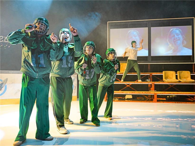 Gemischtes Ensemble des Staatstheaters Mainz auf Bühne als Eishockey-Feld mit Brigitte Urhausen als Hélène