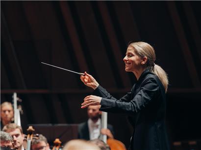 Dirigentin Karina Canellakis bei einem Auftritt in der Philharmonie mit Taktstock und Orchester im Hintergrund