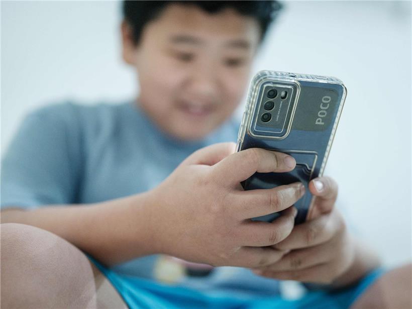 11-jähriger Junge lacht und nutzt Social-Media-Plattform auf Smartphone, fröhlich und aktiv online unterwegs