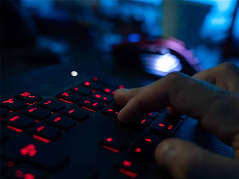 Mann im dunklen Raum tippt konzentriert auf beleuchteter Tastatur – Arbeiten im Homeoffice bei Nacht