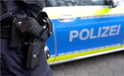 Polizist in Uniform steht vor blau-weißem Polizeieinsatzfahrzeug auf Straße bei Tag