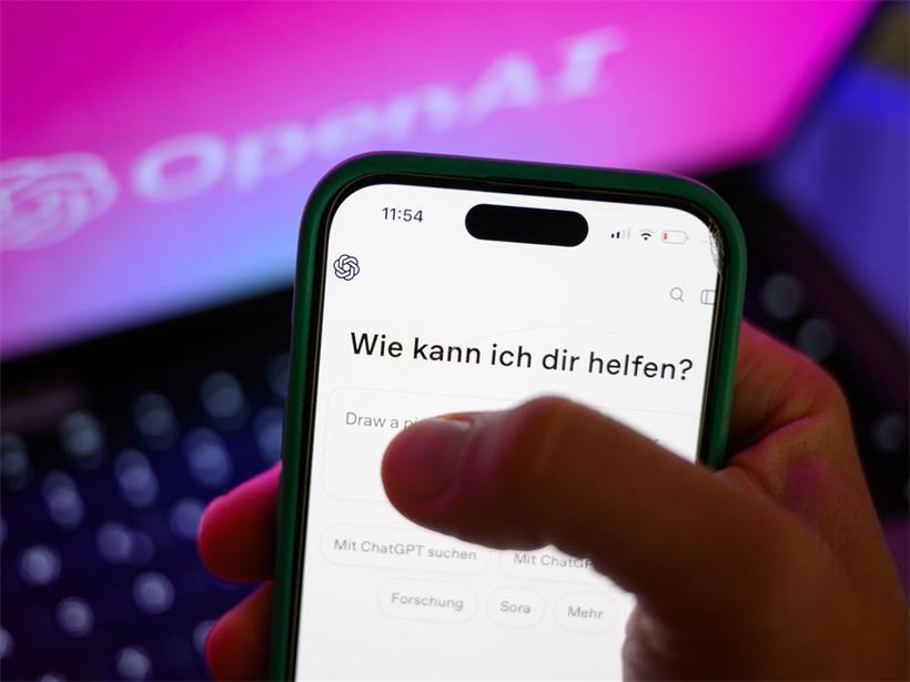 Ein Smartphone mit dem KI-Chatbot ChatGPT ist vor dem Logo des US-Softwareunternehmens OpenAI zu sehen