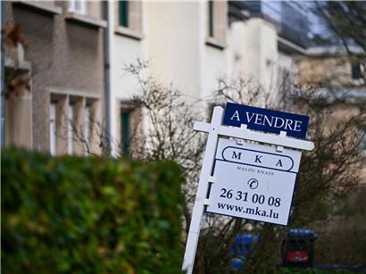 Verkaufsschild vor einem Haus in Luxemburg mit grünem Garten, Immobilienangebot in Luxemburg Stadt