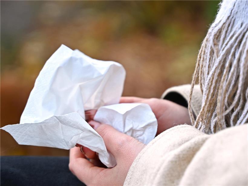Frau sitzt auf Parkbank im Park und hält ein Taschentuch, entspannte Outdoor-Szene bei Tageslicht