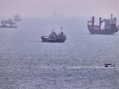 Ein kleines Boot segelt an Frachtschiffen und anderen Handelsschiffen vorbei, die in der Straße von Hormus vor Bandar Abbas im Iran vor Anker liegen