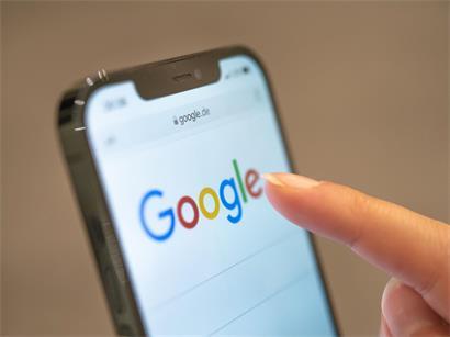 Eine Frau hält ihr Handy in der Hand, auf dem die Google-Seite im Browser zu sehen ist