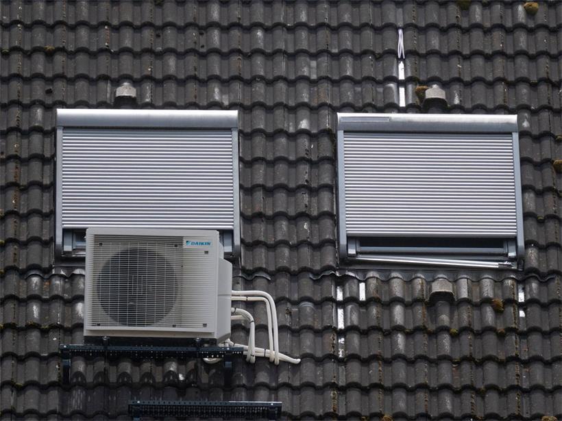 Eine Klimaanlage ist am Dach eines Wohngebäudes unter Dachfenstern zu sehen