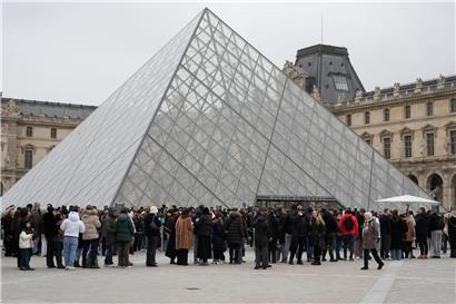 Menschenmenge steht in Warteschlange vor dem historischen Louvre Museum in Paris bei klarem Himmel