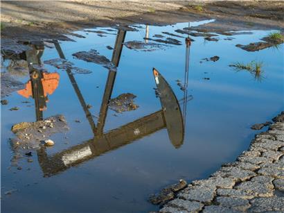 Öl-Pumpe spiegelt sich klar in einer Pfütze auf dem Industriegelände bei Sonnenuntergang