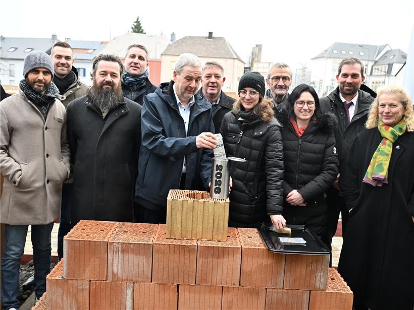 Bürgermeister Michel Wolter versteckt kleine Zeitkapsel im Baustein beim offiziellen Spatenstich