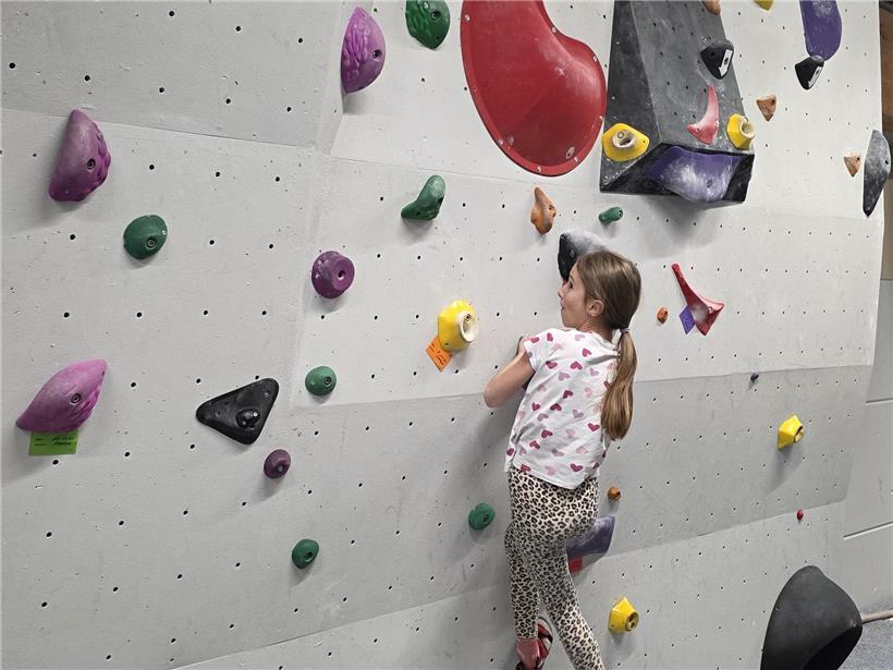 Mädchen Eline klettert begeistert an Kletterwand, zeigt Freude an vielfältigen Hobbys und Bewegung draußen