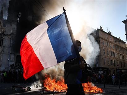 Frankreich, Marseille: Ein Demonstrant, der eine französische Nationalflagge schwenkt, geht während Zusammenstößen vor Beginn einer Demonstration gegen die „hohen Lebenshaltungskosten“ an einem Feuer vorbei. Die Aktion ist Teil eines landesweiten Mobilisierungsaufrufs, der verschiedene Gruppen zusammenbringt.