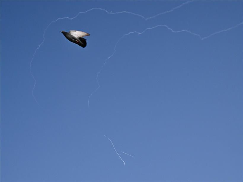Friedenstaube fliegt vor blauem Himmel über Dubai mit Rauchspuren abgefangener iranischer Raketen.