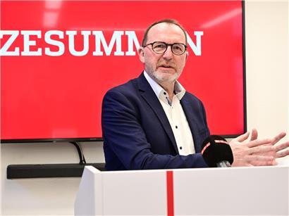 Georges Engel spricht bei einer Pressekonferenz vor Mikrofonen und Medienvertretern.