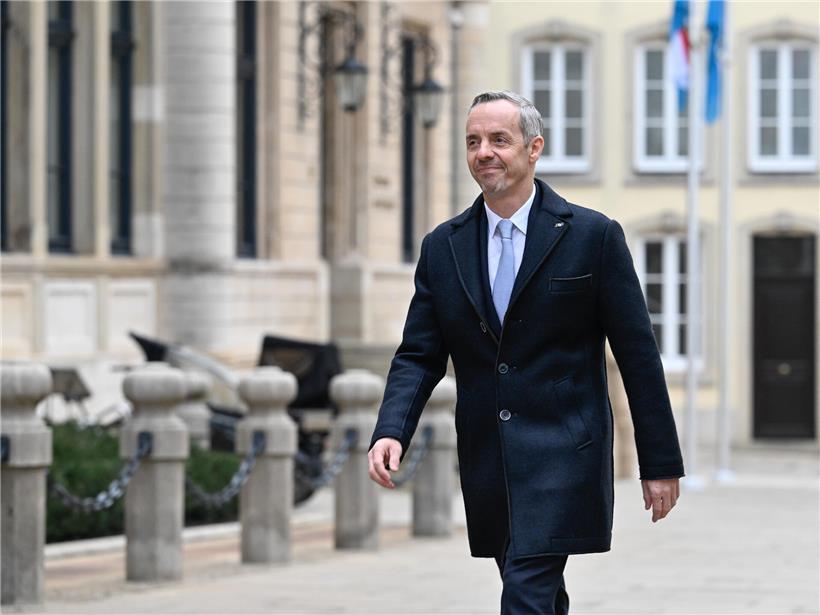 Georges Mischo steht vor dem historischen Parlamentsgebäude bei klarem Himmel, symbolisch für Politik und Demokratie.