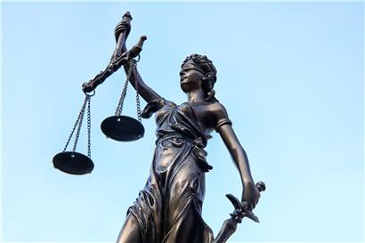 Justitia-Statue mit Waage und Schwert, Symbol für Gerechtigkeit und Rechtsprechung vor blauem Hintergrund