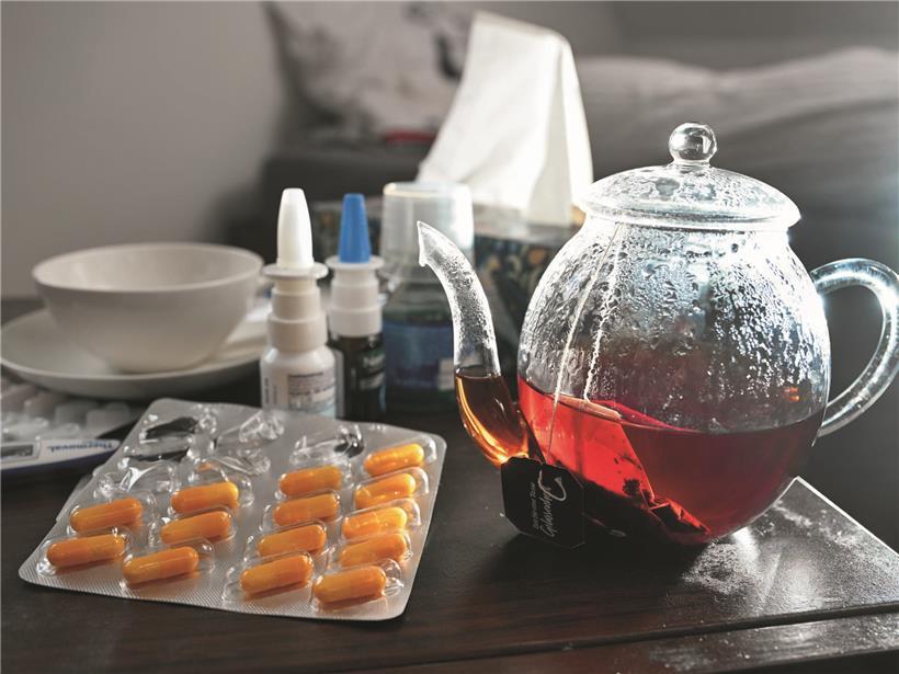 Medikamente, Kanne und Tasse Tee auf Nachttisch zur Erkältungsbehandlung und Linderung von Symptomen