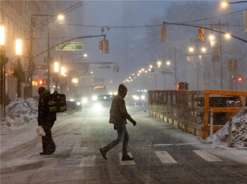 Menschen laufen durch verschneite Stadtstraße im Schneesturm, während Stadt sich auf Winterwetter vorbereitet