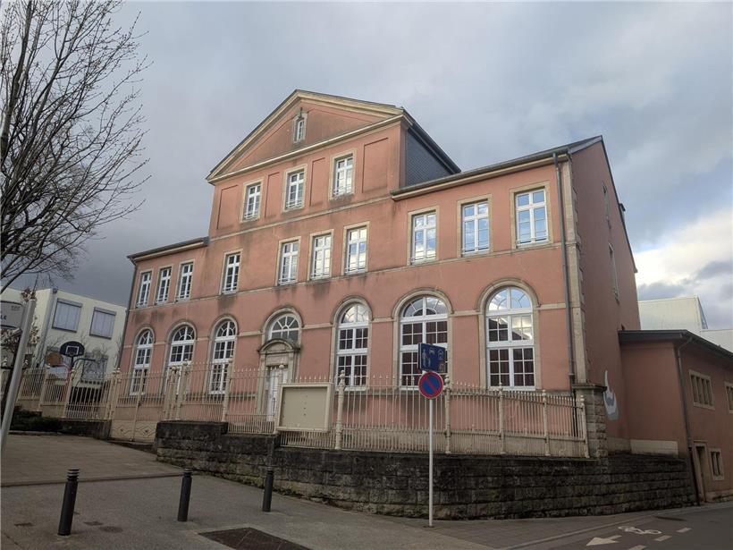 Historische Steine des alten Turms neben moderner Schulgebäude-Fassade im Vergleich heute